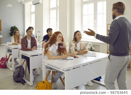 High school students listen attentively to bearded professor. Modern classroom interior. 98783645