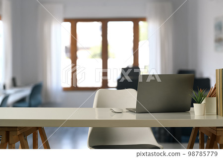 Comfortable home office interior with laptop computer, pencil holder, coffee cup and potted plant on white table 98785779