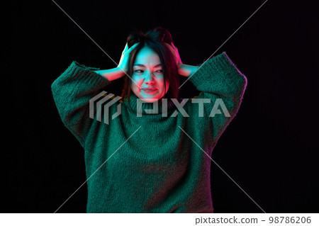 Questioning mood, grimacing. Young girl in cozy sweater over dark background in neon light. Concept of emotions, youth lifestyle Questioning mood, grimacing. Young girl in cozy sweater over dark background in neon light. Concept of emotions, youth lifestyle 98786206