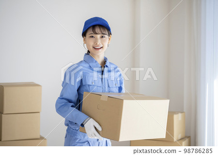 A young woman in work clothes holding a cardboard box image of a moving company 98786285