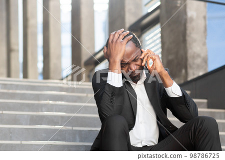 An upset African American man in a suit sits on the steps of a courthouse. Talking worriedly on the phone, holding his head. Lost the case, has problems An upset African American man in a suit sits on the steps of a courthouse. Talking worriedly on the phone, holding his head. Lost the case, has problems 98786725