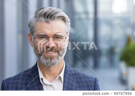 Successful gray haired man in business suit close up, portrait of mature businessman with beard and glasses, banker investor smiling and looking at camera from outside office building boss satisfied. 98787998