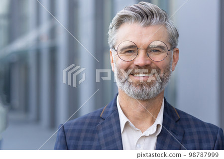 Successful gray haired man in business suit close up, portrait of mature businessman with beard and glasses, banker investor smiling and looking at camera from outside office building boss satisfied. 98787999