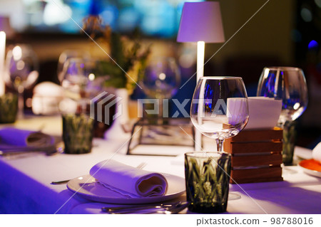 a table with a white tablecloth, glasses, crockery and decor in dark restaurant a table with a white tablecloth, glasses, crockery and decor in dark restaurant 98788016