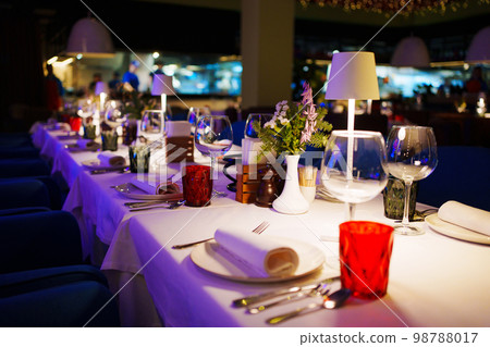 a table with a white tablecloth, glasses, crockery and decor in dark restaurant 98788017