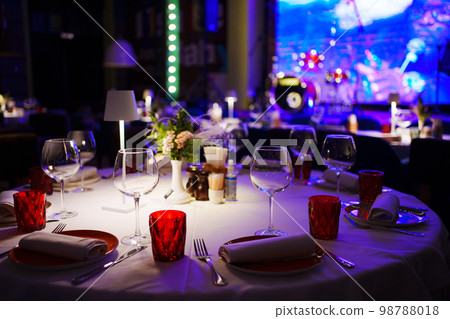 a table with a white tablecloth, glasses, crockery and decor in dark restaurant a table with a white tablecloth, glasses, crockery and decor in dark restaurant 98788018