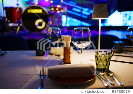 a table with a white tablecloth, glasses, crockery and decor in dark restaurant a table with a white tablecloth, glasses, crockery and decor in dark restaurant 98788019