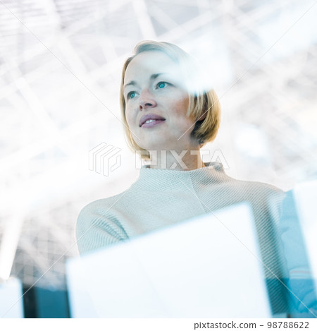 Portrait of strong, determined, successful young woman looking trough window while waiting to board an airplane at airport terminal departure gates 98788622