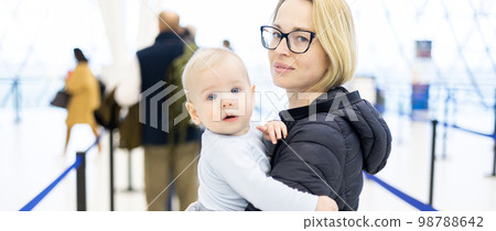 Mother holding his infant baby boy child queuing at airport terminal in passport control line at immigrations departure before moving to boarding gates to board an airplane. Travel with baby concept. 98788642