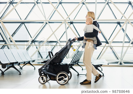 Mother carying his infant baby boy child, pushing stroller at airport departure terminal moving to boarding gates to board an airplane. Family travel with baby concept 98788646
