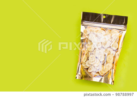 Banana slice chips in package bag on green background. Banana slice chips in package bag on green background. 98788997