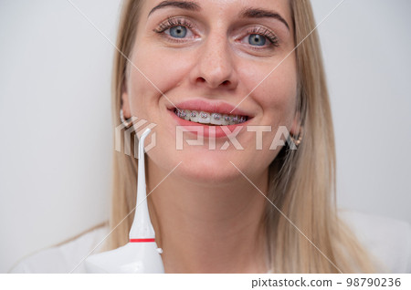 Portrait of a caucasian woman with braces on her teeth holding an irrigator.  98790236
