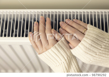 Female hands on a heating radiator, close-up. 98790292