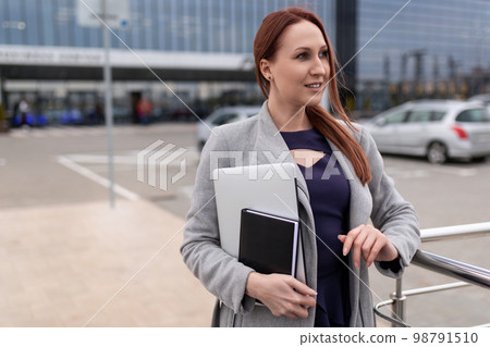 mature red-haired businesswoman with a laptop in her hands in the parking lot of a business center mature red-haired businesswoman with a laptop in her hands in the parking lot of a business center 98791510