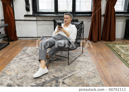 caucasian woman with a short haircut looks at the screen of the phone Sitting in a chair 98791511