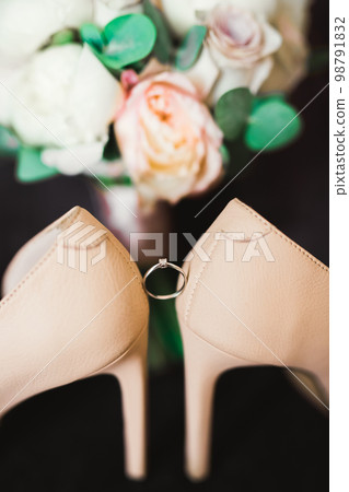 Pair of elegant and stylish bridal shoes with wedding rings and a bouquet of roses and other flowers Pair of elegant and stylish bridal shoes with wedding rings and a bouquet of roses and other flowers 98791832