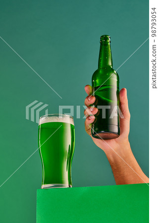 Popular and favorite drink. Glass and bottle of green foamy beer over green background. Concept of st patrick's day celebration, brewery, traditions Popular and favorite drink. Glass and bottle of green foamy beer over green background. Concept of st patrick's day celebration, brewery, traditions 98793054