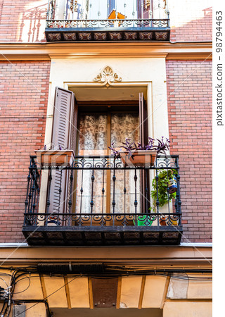 Traditional iron balcony with pots hanging from the railing Traditional iron balcony with pots hanging from the railing 98794463