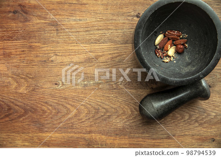 Top angle view of various nuts in stone mortar on a wooden shelf background, almonds, hazelnuts, walnuts dried top view and copy space Top angle view of various nuts in stone mortar on a wooden shelf background, almonds, hazelnuts, walnuts dried top view and copy space 98794539