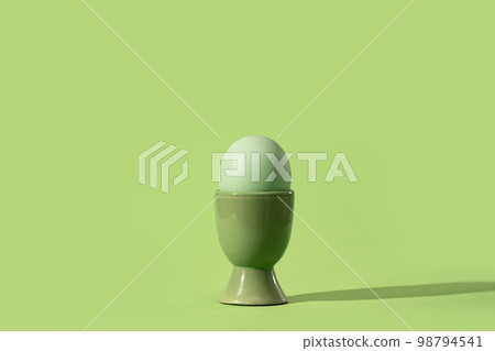 Dyed easter egg in matching egg cup on green. Minimal monochrome Happy Easter concept card Dyed easter egg in matching egg cup on green. Minimal monochrome Happy Easter concept card 98794541