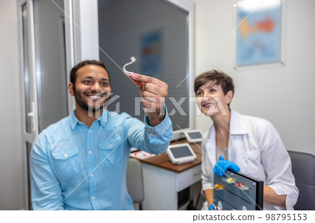 ENT doctor demonstrating hearing aid models to the patient 98795153
