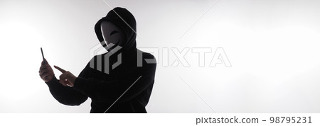 Hacker Anonymous and face mask with smartphone in hand. Man in black hood shirt holding and using mobile phone on white background. Represent cyber crime data hacking or stealing personal data concept Hacker Anonymous and face mask with smartphone in hand. Man in black hood shirt holding and using mobile phone on white background. Represent cyber crime data hacking or stealing personal data concept 98795231