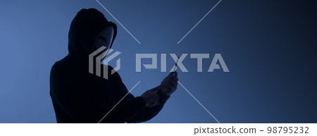 Hacker Anonymous and face mask with smartphone in hand. Man in black hood shirt holding and using mobile phone on white background. Represent cyber crime data hacking or stealing personal data concept Hacker Anonymous and face mask with smartphone in hand. Man in black hood shirt holding and using mobile phone on white background. Represent cyber crime data hacking or stealing personal data concept 98795232