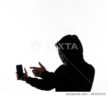 Hacker Anonymous and face mask with smartphone in hand. Man in black hood shirt holding and using mobile phone on white background. Represent cyber crime data hacking or stealing personal data concept 98795259