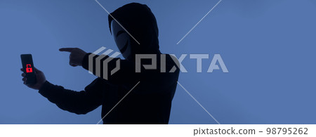 Hacker Anonymous and face mask with smartphone in hand. Man in black hood shirt holding and using mobile phone on white background. Represent cyber crime data hacking or stealing personal data concept Hacker Anonymous and face mask with smartphone in hand. Man in black hood shirt holding and using mobile phone on white background. Represent cyber crime data hacking or stealing personal data concept 98795262