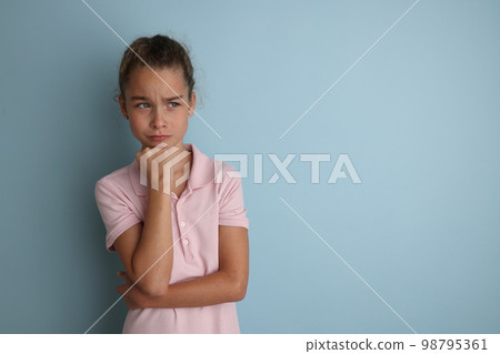 Little emotional teenage girl in pink shirt 11, 12 years old on an isolated blue background. Children's studio portrait. Place text to copy space for caption, advertising children's goods. Little emotional teenage girl in pink shirt 11, 12 years old on an isolated blue background. Children's studio portrait. Place text to copy space for caption, advertising children's goods. 98795361