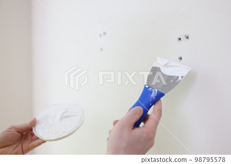 Hands with a spatula and putty near the wall, close-up 98795578