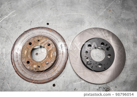 Old rusty brake disc and new disc. Change the old to new brake disc on car in a garage. Auto repair concept. Old rusty brake disc and new disc. Change the old to new brake disc on car in a garage. Auto repair concept. 98796054