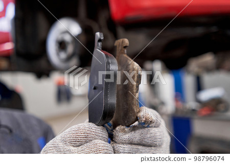 The mechanic holds the old and new brake pads in his hand. Change the old to new brake disc on car in a garage. Auto repair concept. The mechanic holds the old and new brake pads in his hand. Change the old to new brake disc on car in a garage. Auto repair concept. 98796074