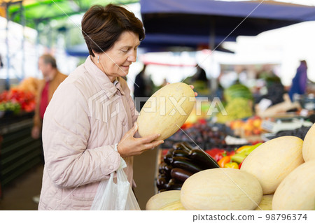 Aged woman customer buying melon in open-air market 98796374