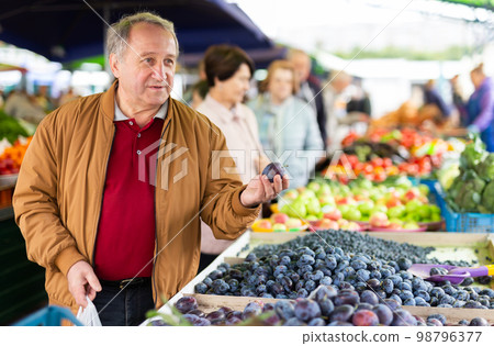 Aged man customer buying plums in open-air market 98796377