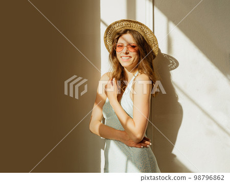 Happy lady in summer outfit, dress, straw hat and colorful sunglasses smiling at camera while enjoying the sunlight Happy lady in summer outfit, dress, straw hat and colorful sunglasses smiling at camera while enjoying the sunlight 98796862