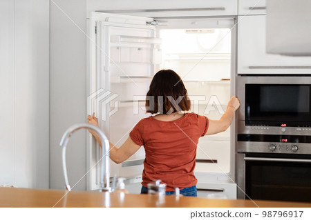Young Woman Standing In Kitchen And Looking Inside Of Empty Fridge Young Woman Standing In Kitchen And Looking Inside Of Empty Fridge 98796917