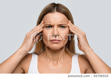 Irritated blonde middle aged woman rubbing her temples Irritated blonde middle aged woman rubbing her temples 98796930