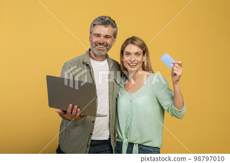 Online shopping and e-commerce. Happy middle aged caucasian man holding laptop, woman showing credit card Online shopping and e-commerce. Happy middle aged caucasian man holding laptop, woman showing credit card 98797010