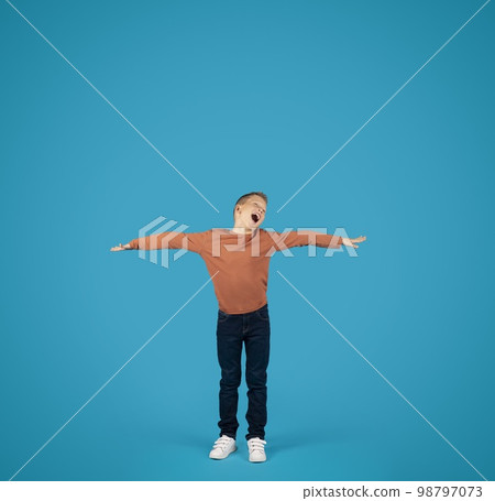 Cheerful Preteen Boy Spreading Hands, Pretending Flying Over Blue Background 98797073