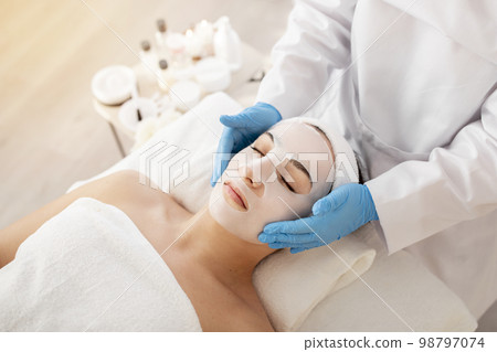 Cosmetology. Beautician doctor applying face mask to young woman in spa salon 98797074
