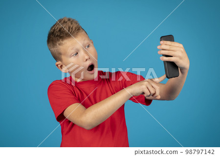Portrait of scared preteen boy using smartphone and opening mouth in shock Portrait of scared preteen boy using smartphone and opening mouth in shock 98797142