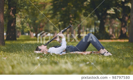 A girl plays the clarinet while lying on the grass in the park. A girl plays the clarinet while lying on the grass in the park. 98797580