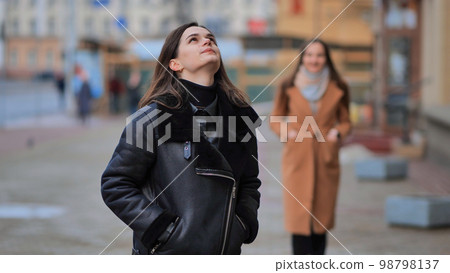 A friend comes up from behind her waiting girlfriend on a city street. 98798137