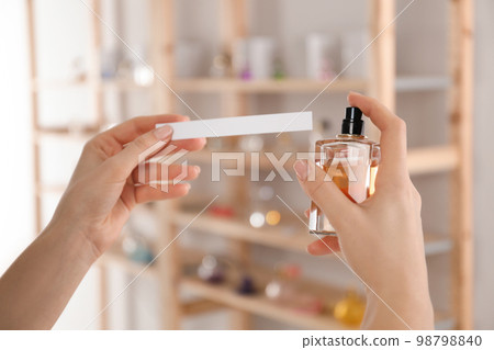 Woman with bottle of perfume and blotter indoors, closeup 98798840