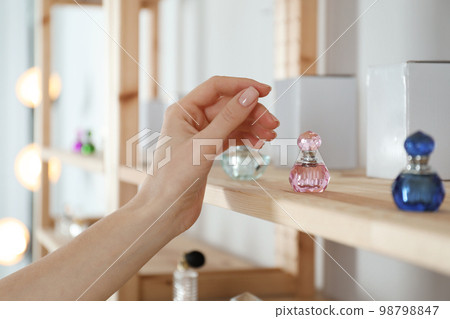 Woman taking bottle of perfume from wooden shelf indoors, closeup 98798847