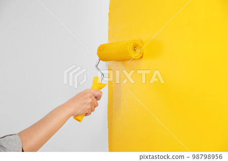 Woman painting white wall with yellow dye, closeup. Interior renovation Woman painting white wall with yellow dye, closeup. Interior renovation 98798956