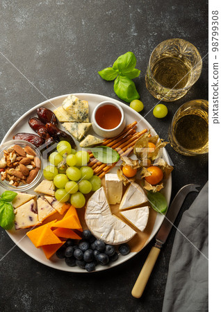 Cheese plate with various cheeses, fruits, nuts and snacks. Dark background. Cheese plate with various cheeses, fruits, nuts and snacks. Dark background. 98799308