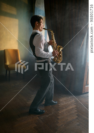 Young elegant man playing gold alto saxophone in misty room 98801716