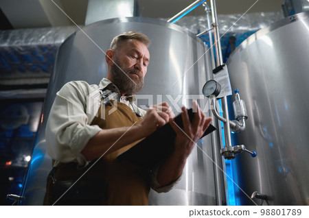 Handsome bearded man brewer inside modern beer factory around steel tanks 98801789